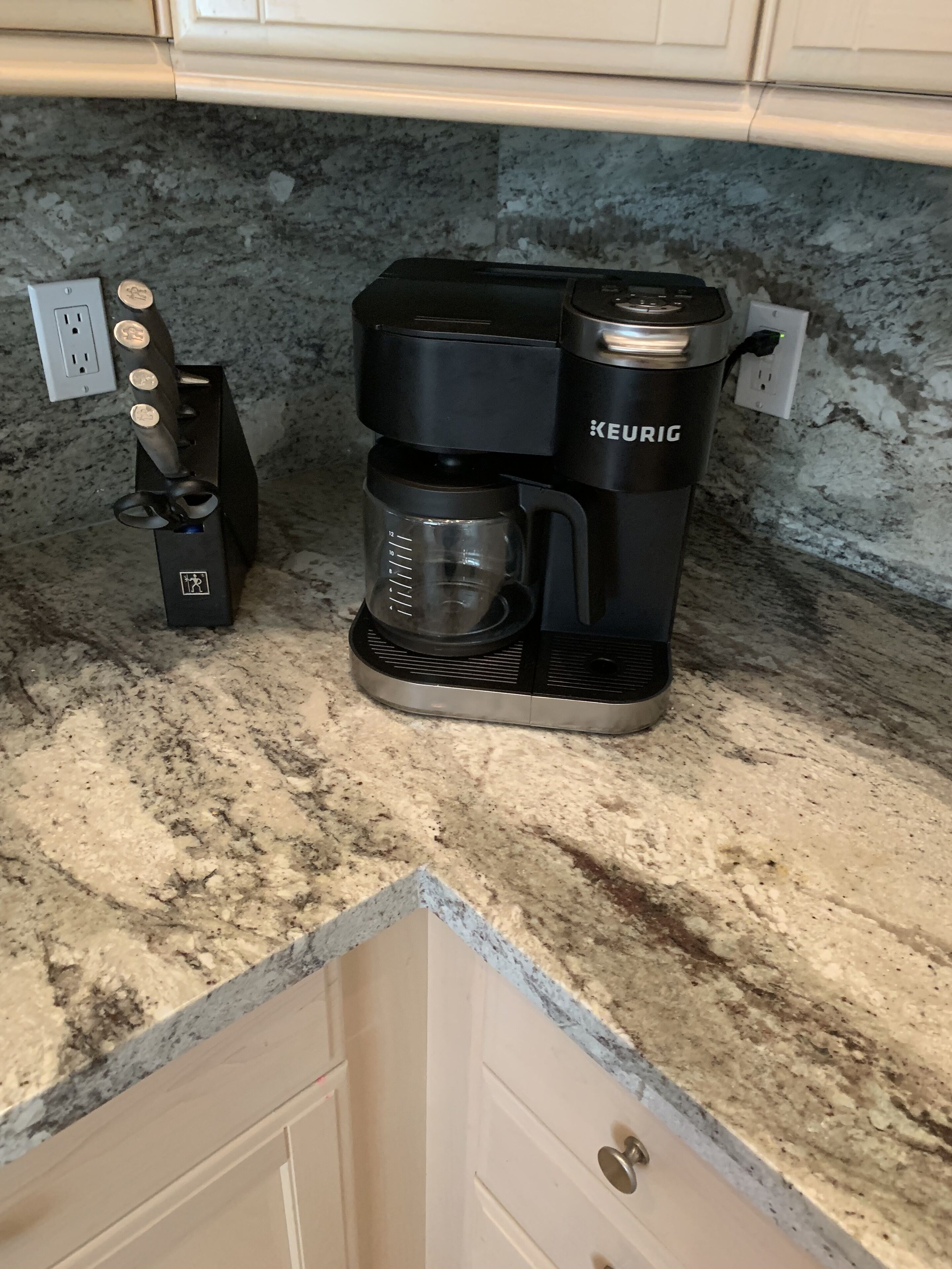 A Keurig coffee maker on a granite countertop with a coffee pod holder and a coffee pot.