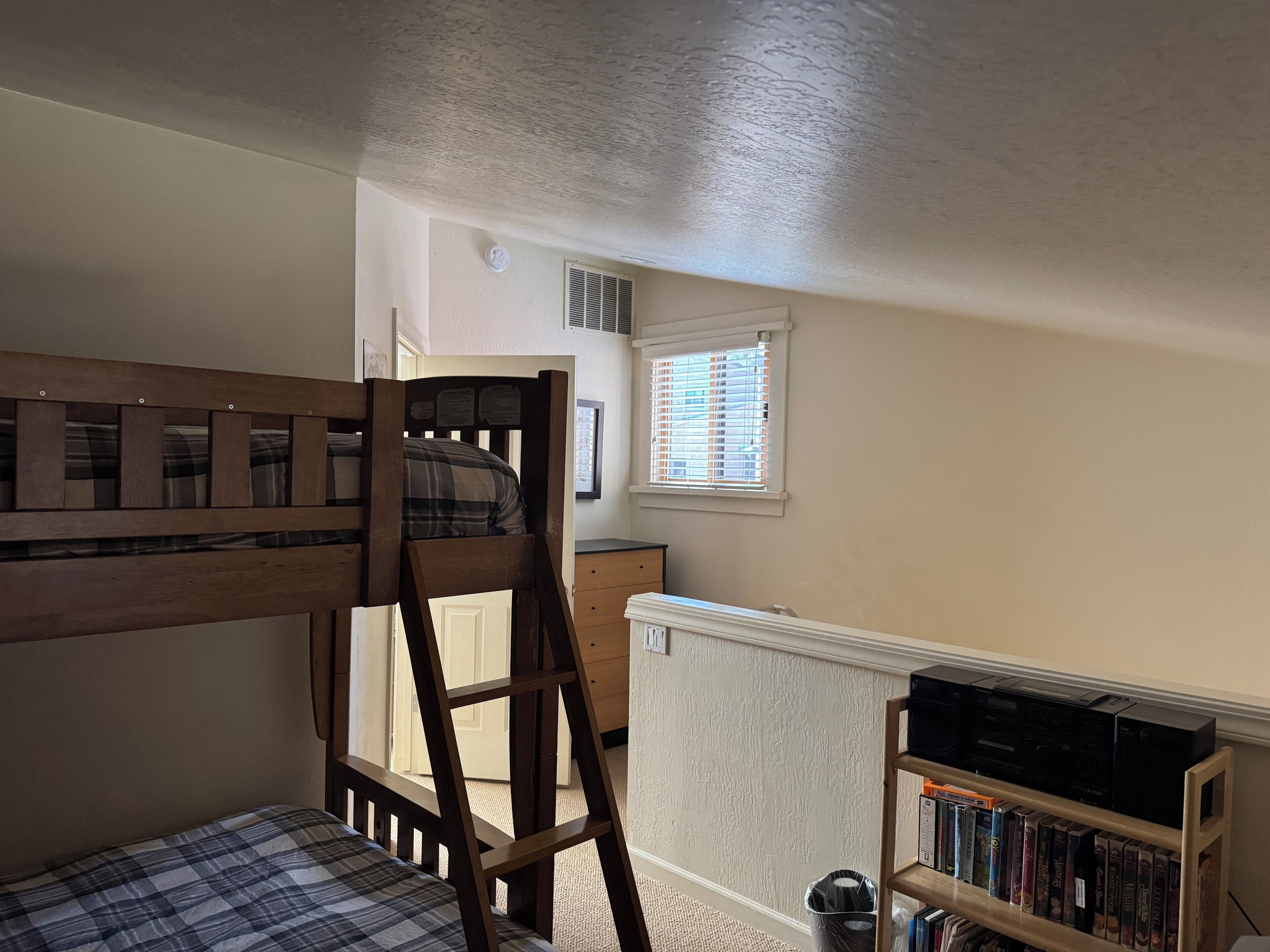 A bunk bed with a ladder, a small desk, a radiator, and a bookshelf with books.