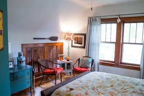 Een slaapkamer met een bed, een stoel, een dressoir, een lamp en een raam met gordijnen.