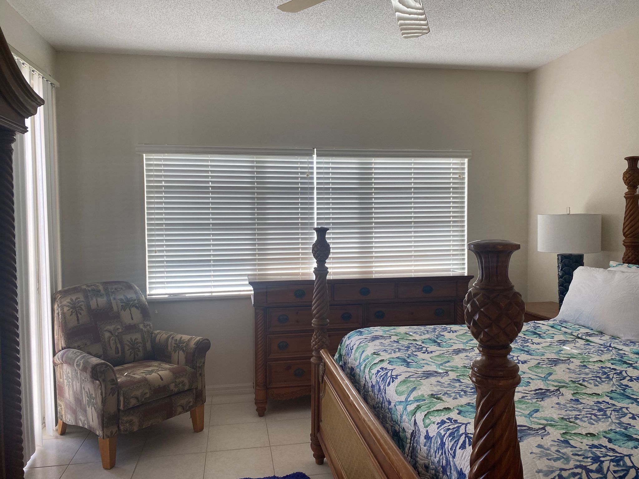 A bedroom with a bed, a chair, a dresser, and a window with blinds.