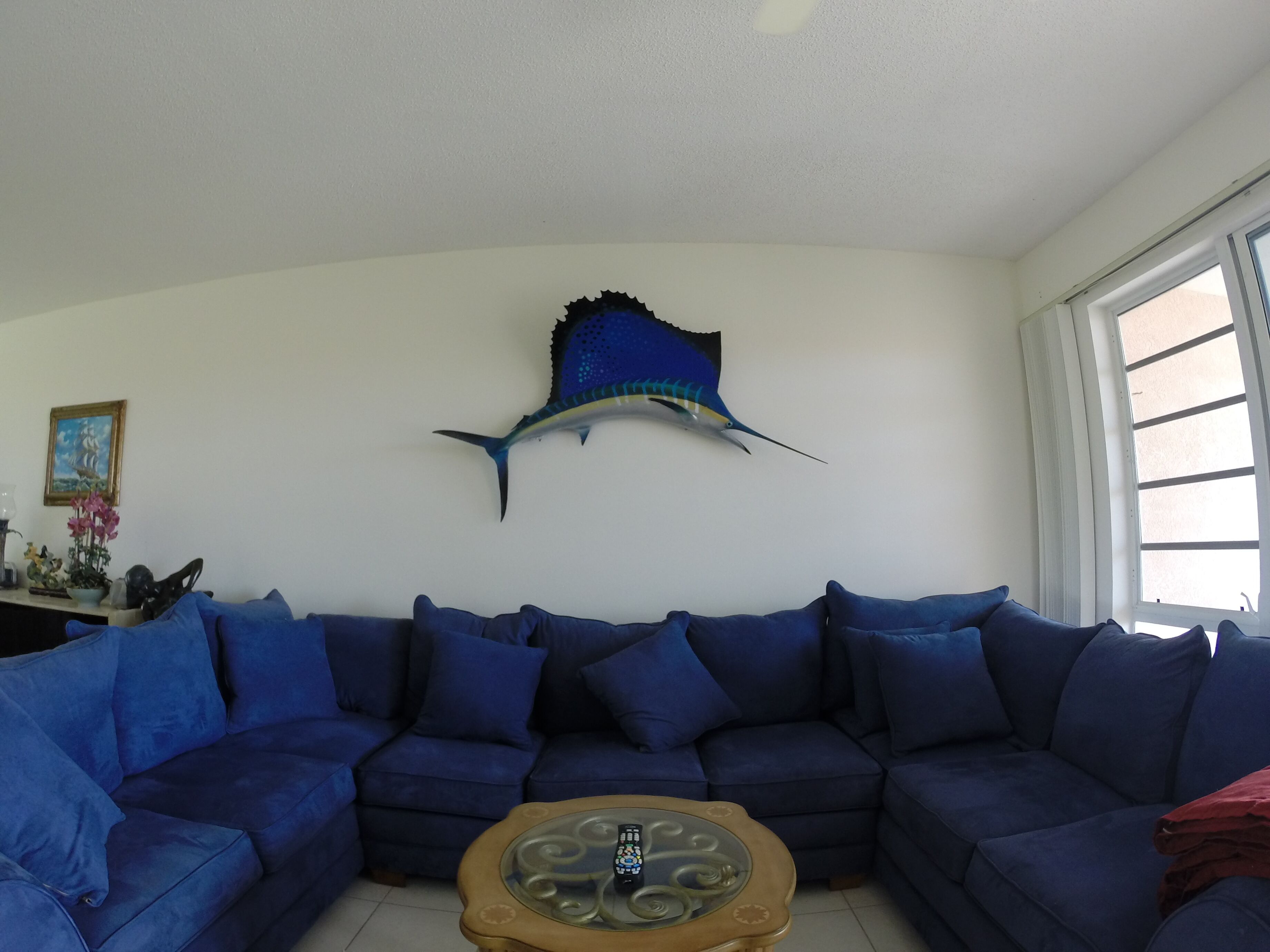 Un salon avec un canapé bleu, une table basse en verre et une décoration murale représentant des poissons.
