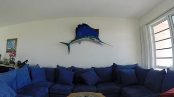 Un salon avec un canapé bleu, une table basse en verre et une décoration murale représentant des poissons.