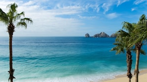 Une plage bordée d’une eau turquoise et limpide, de palmiers et de formations rocheuses lointaines, le tout sous un ciel bleu.