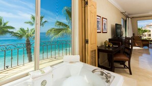 Une chambre dotée d’une grande baignoire, d’un coin repas avec une table et des chaises, et offrant une vue sur l’océan depuis un balcon avec une balustrade.