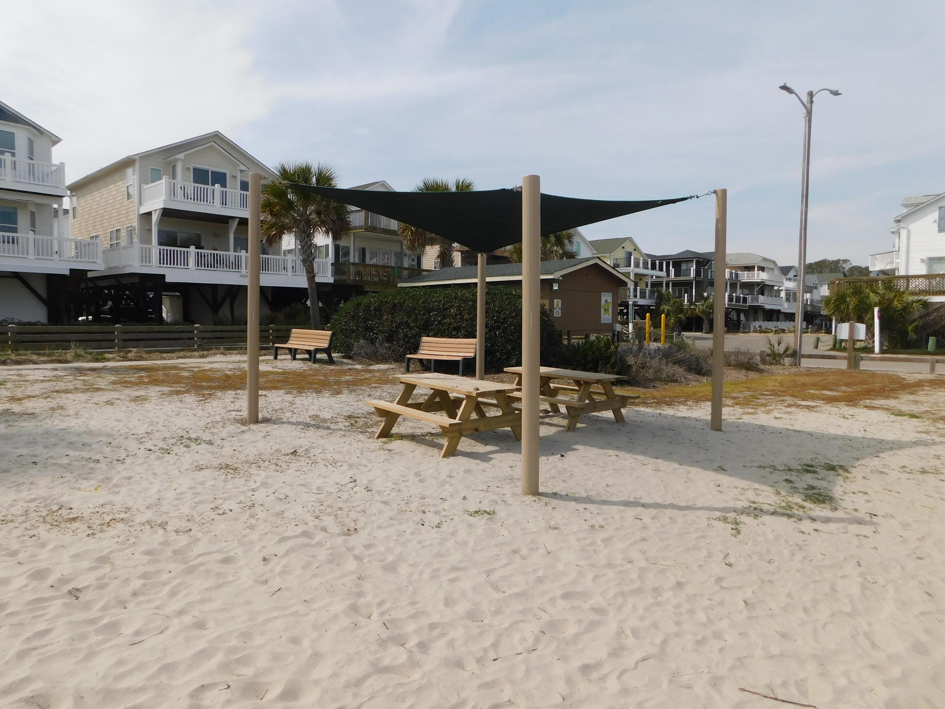 A beach area with picnic tables, a shaded area, and beachfront houses.