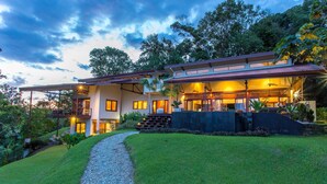 A modern house with a covered patio, a gravel pathway, and lush greenery.