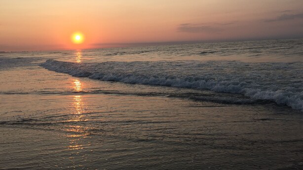 Un atardecer sobre una playa con olas acariciando suavemente la orilla.