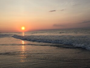 Un coucher de soleil sur une plage, avec des vagues qui viennent doucement lécher le rivage.