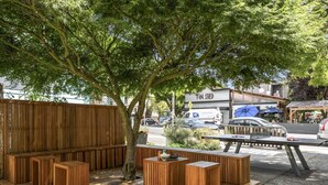 A wooden deck with seating, a tree, and a building labeled "Tin Shed" in the background. - Thoughtfully Styled, Family- and Pet-Friendly Home in a Walkable Area (Portland)