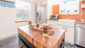 A modern kitchen with a wooden countertop, stainless steel appliances, and a window with blue curtains. - Thoughtfully Styled, Family- and Pet-Friendly Home in a Walkable Area (Portland)