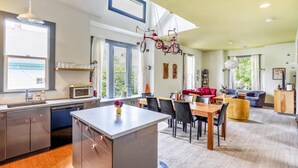 A modern kitchen with a central island, dining area with chairs, a red sofa, and a TV. - Thoughtfully Styled, Family- and Pet-Friendly Home in a Walkable Area (Portland)