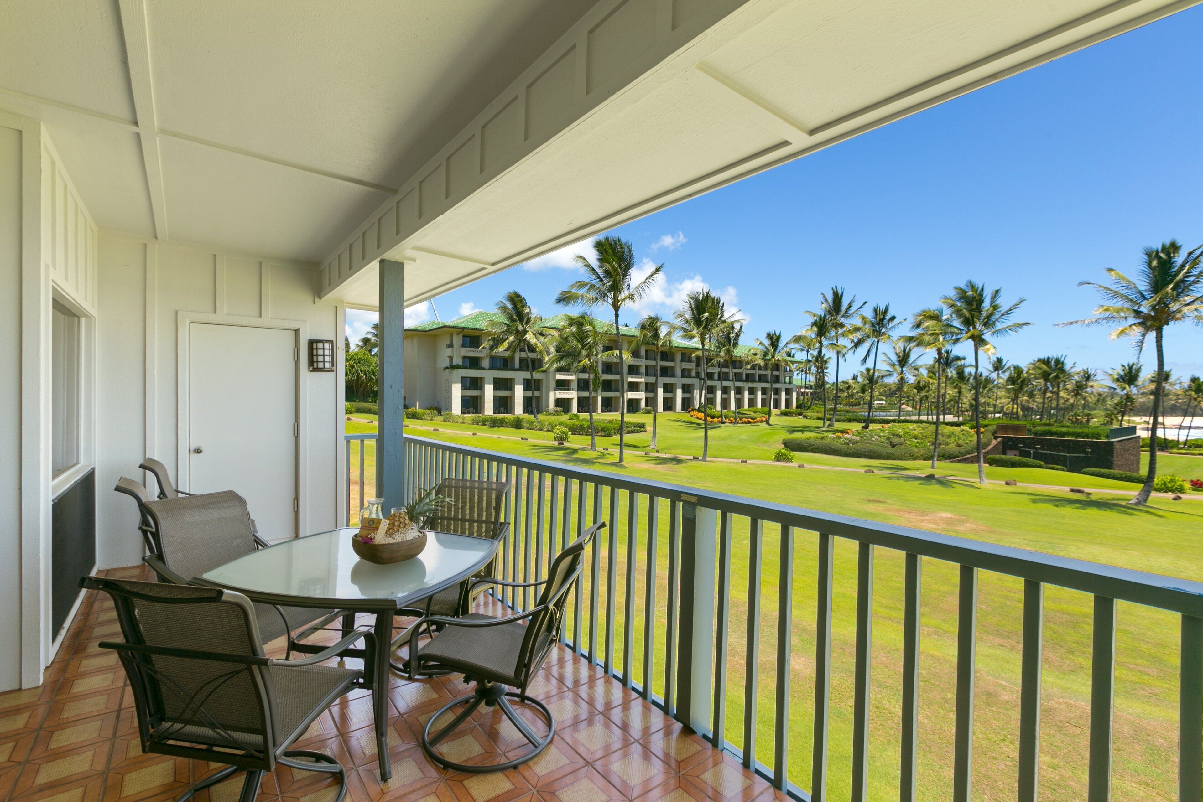 A balcony with a table and chairs, overlooking a well-maintained lawn and a building with multiple floors.