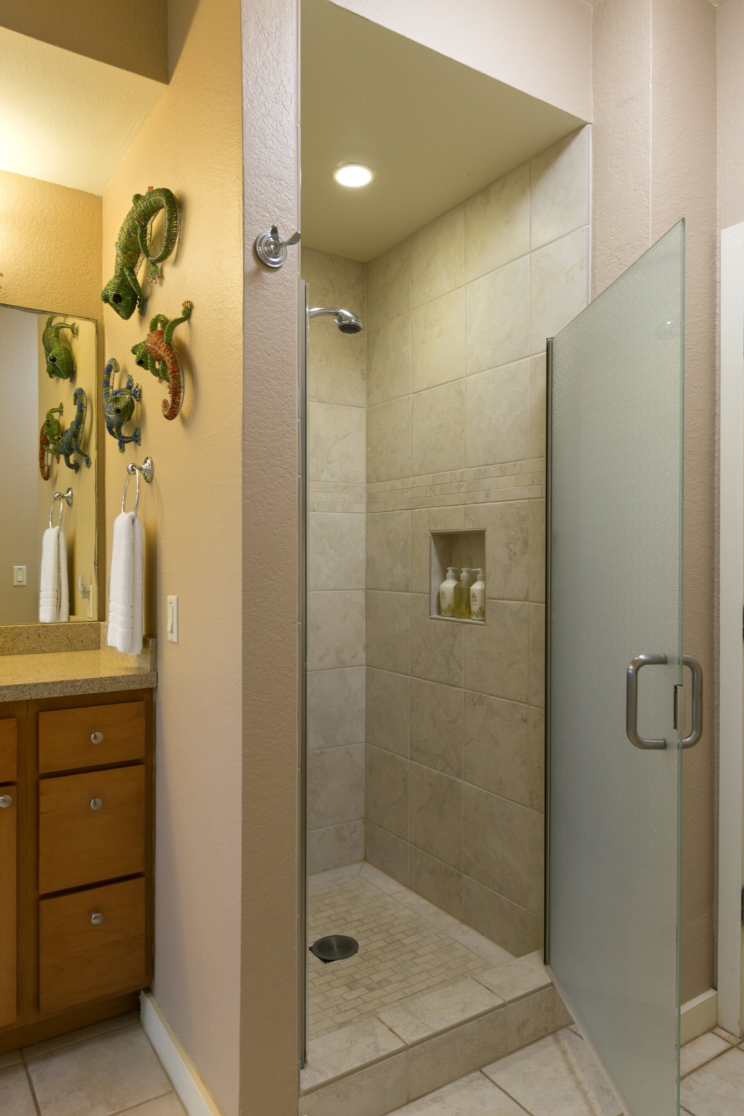 A bathroom with a glass-enclosed shower, beige tiles, a wooden vanity, and decorative wall art.