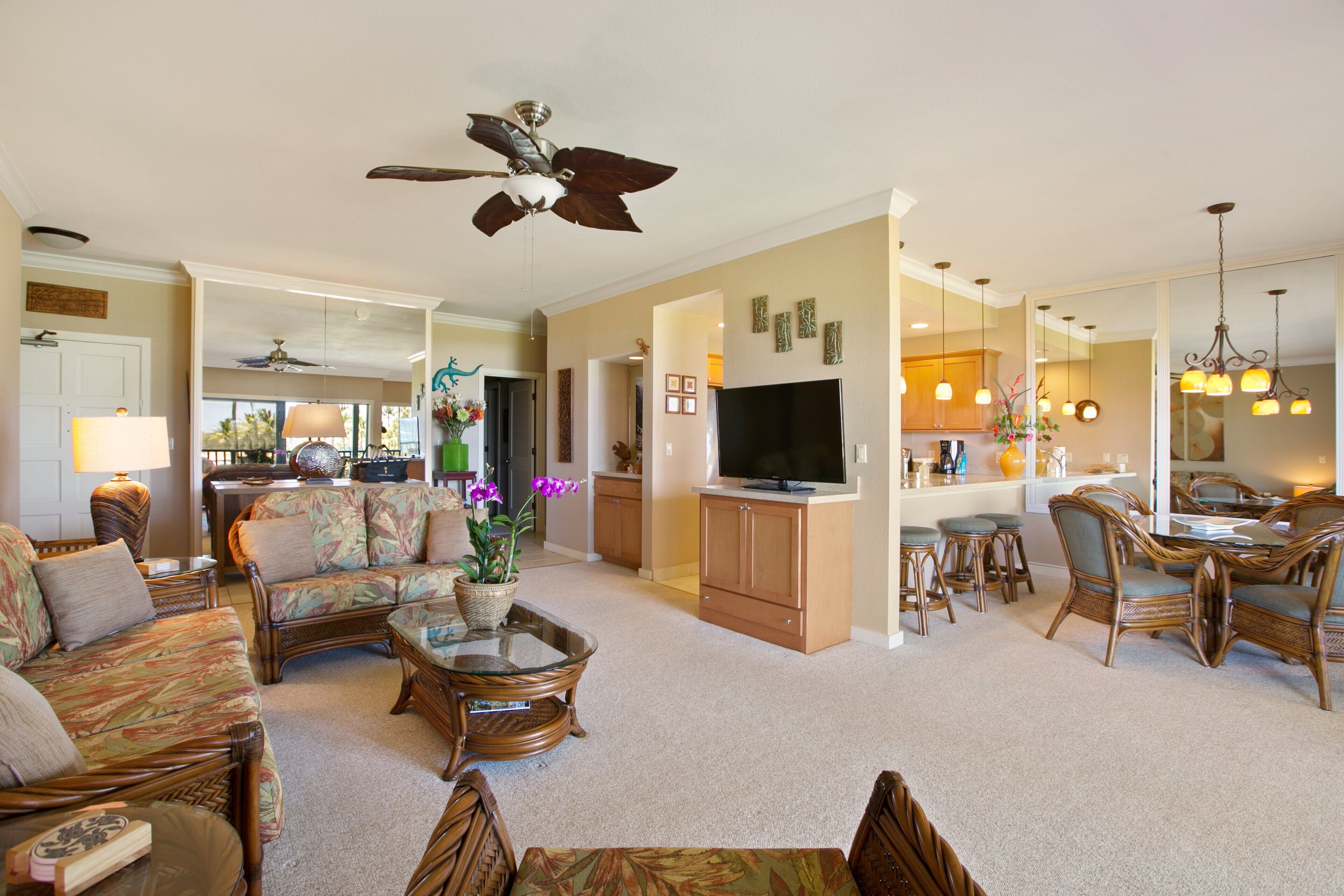 A spacious living room with a ceiling fan, a television, and a dining area with wicker furniture.