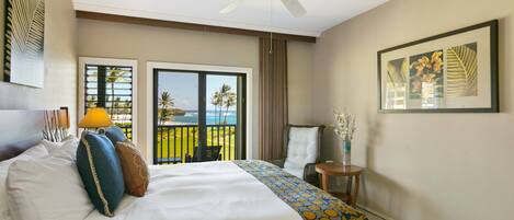 Habitación de hotel con cama, ventilador de techo, balcón con vista a palmeras y un cuadro en la pared.