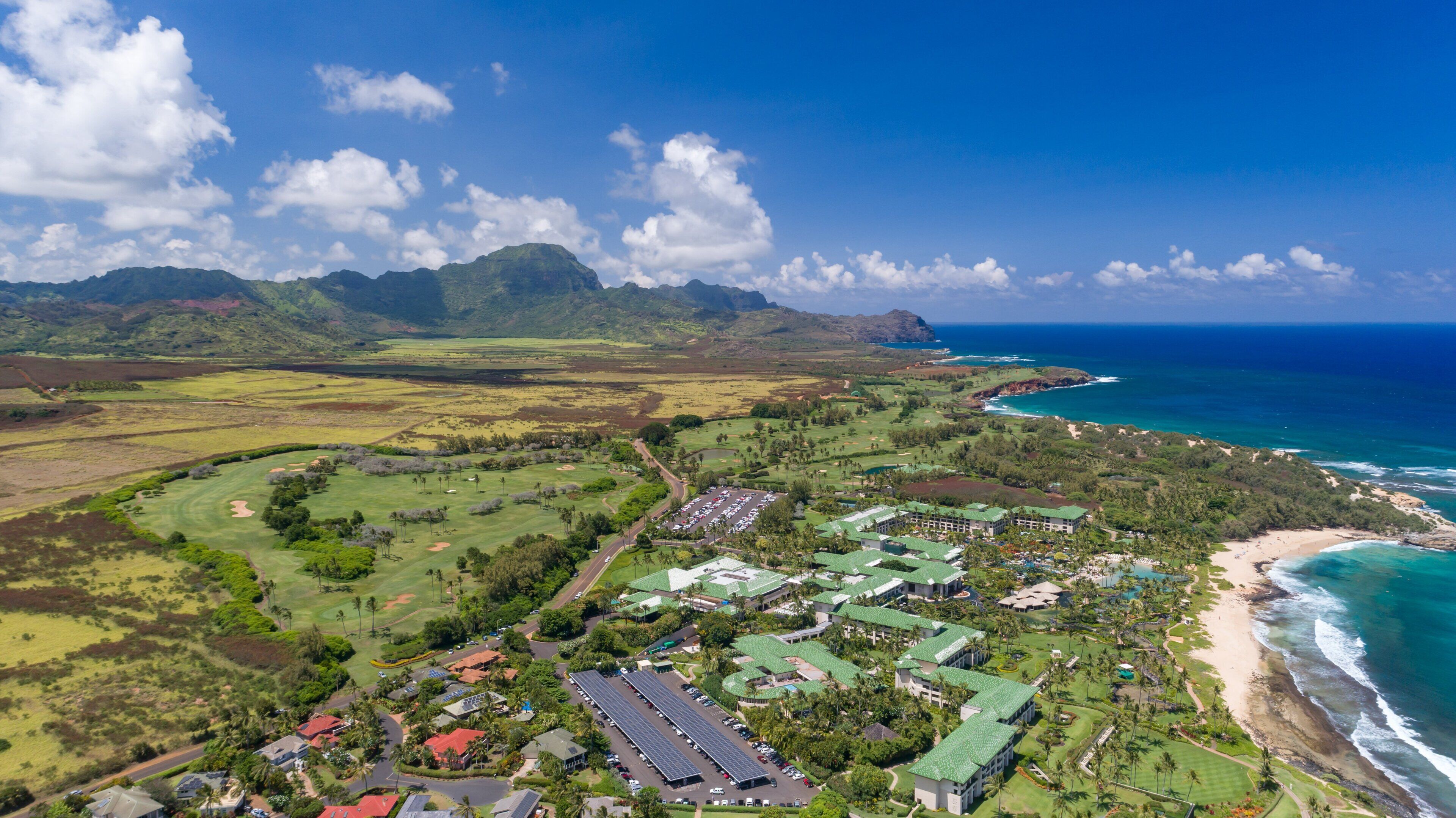 Vista aérea de un complejo turístico en la costa, con campos de golf, una playa y vistas al océano.