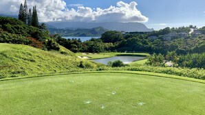A golf course with a pond, lush greenery, and distant mountains. - Serene Mountain View Condo 11B North Shore Princeville - on Makai Golf Course (Princeville)