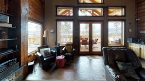 Un salón acogedor con sofás de cuero, una mesa de centro y una chimenea. Amplias ventanas ofrecen vistas al exterior.