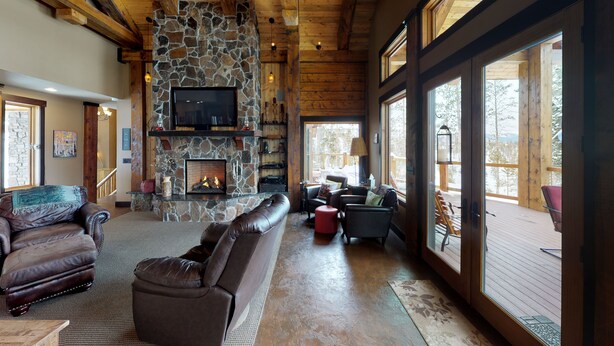 Un salón amplio con chimenea de piedra, sofás de cuero y ventanas grandes que ofrecen vistas al exterior.