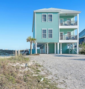 A multi-story building with a balcony, located on a beach with a gravel driveway. - You'll love Seafoam! Beachfront. Pool. 6 BR, sleeps 18. Nice. (Gulf Shores)
