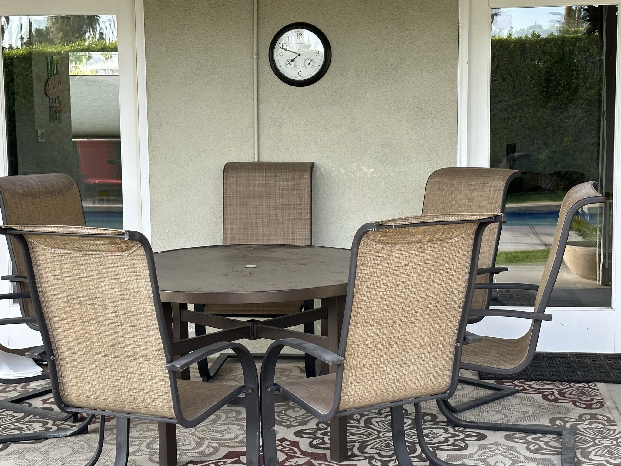 A round table with four chairs, a wall clock, and a view of a pool through glass doors.