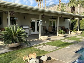Une terrasse couverte, aménagée avec du mobilier d’extérieur, un barbecue et des plantes en pot.