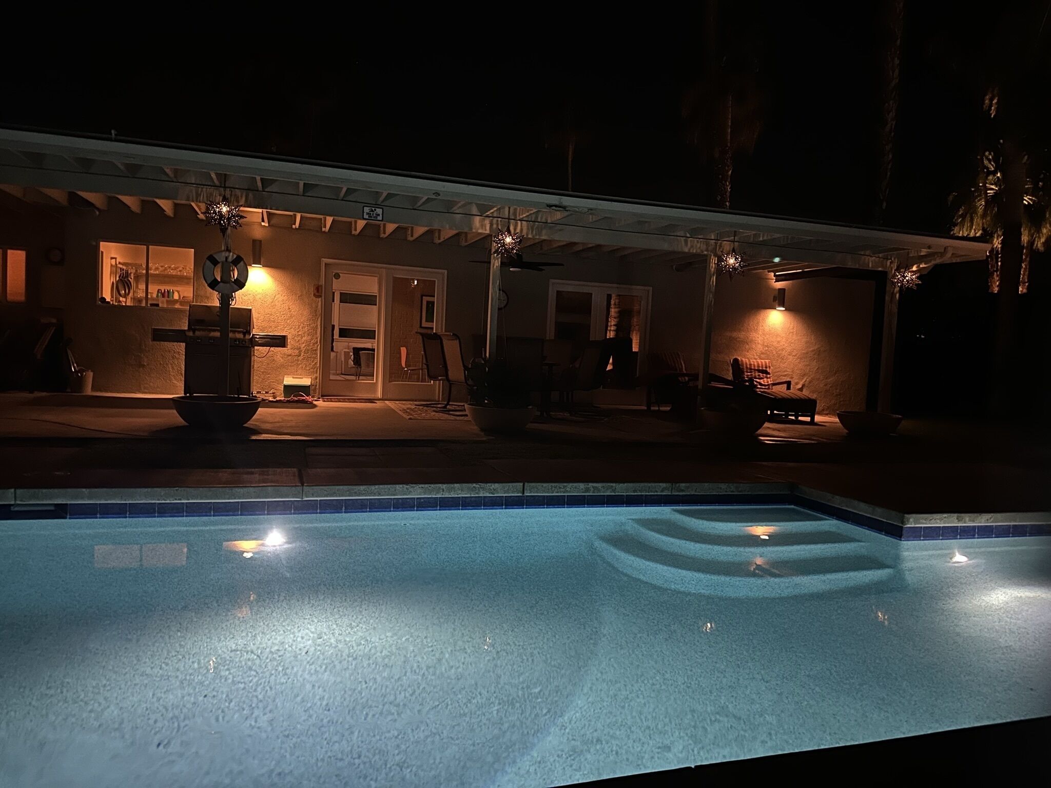 A swimming pool with a covered patio area, a lifebuoy, and a well-lit entrance.