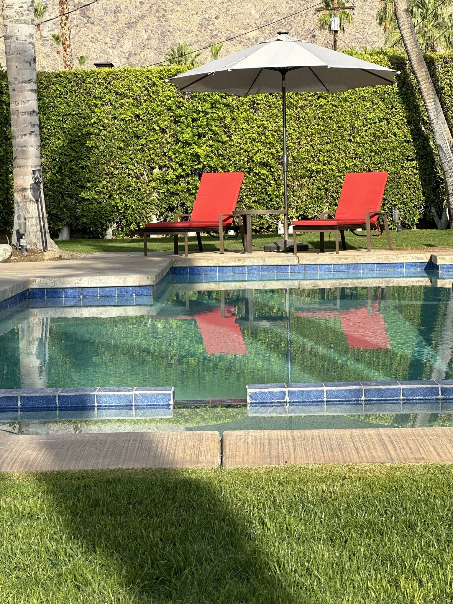 A swimming pool with two red lounge chairs and a large umbrella.