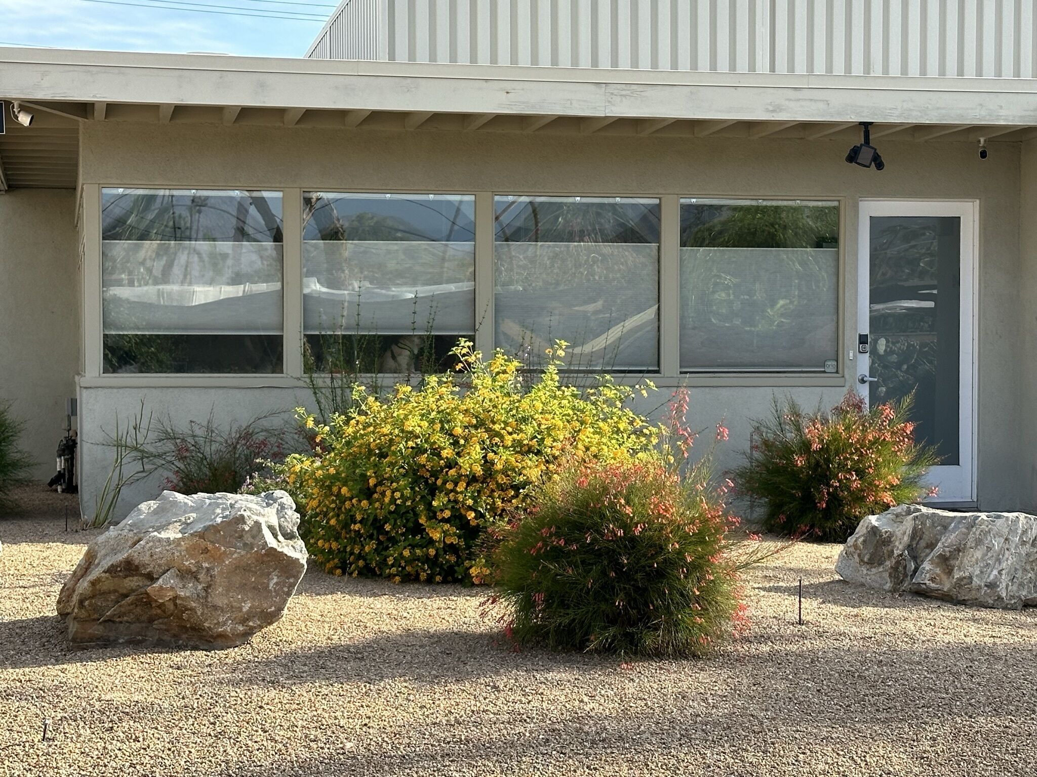 A building with large windows, a door, and a gravel driveway.