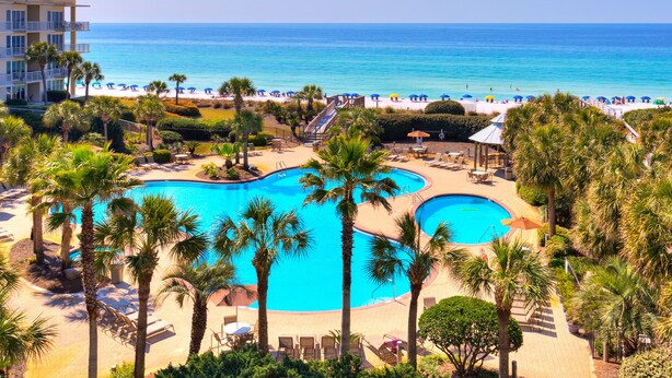 Een resort met een groot zwembad, omringd door palmbomen, een strand en uitzicht op de oceaan.