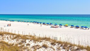 Een strand met wit zand, helder turquoise water en blauwe parasols.