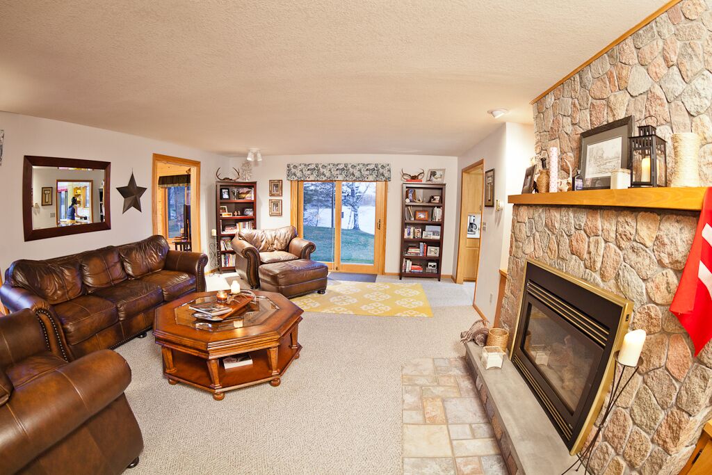 A cozy living room with a stone fireplace, leather sofas, and a large window overlooking a scenic view.