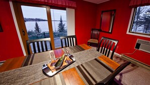 A dining area with a large table, chairs, and a view of a lake and trees through the windows.