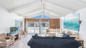 A spacious living area with a large dark sofa, wicker chairs, a flat-screen TV, and a balcony with a view of the ocean. - Upper-Level Ocean View Beach Home, Sunny with Coastal Charm! (Newport Beach)