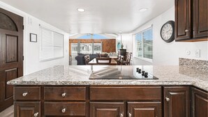 A spacious kitchen with granite countertops, wooden cabinets, and a dining area with a large window. - Upper-Level Ocean View Beach Home, Sunny with Coastal Charm! (Newport Beach)