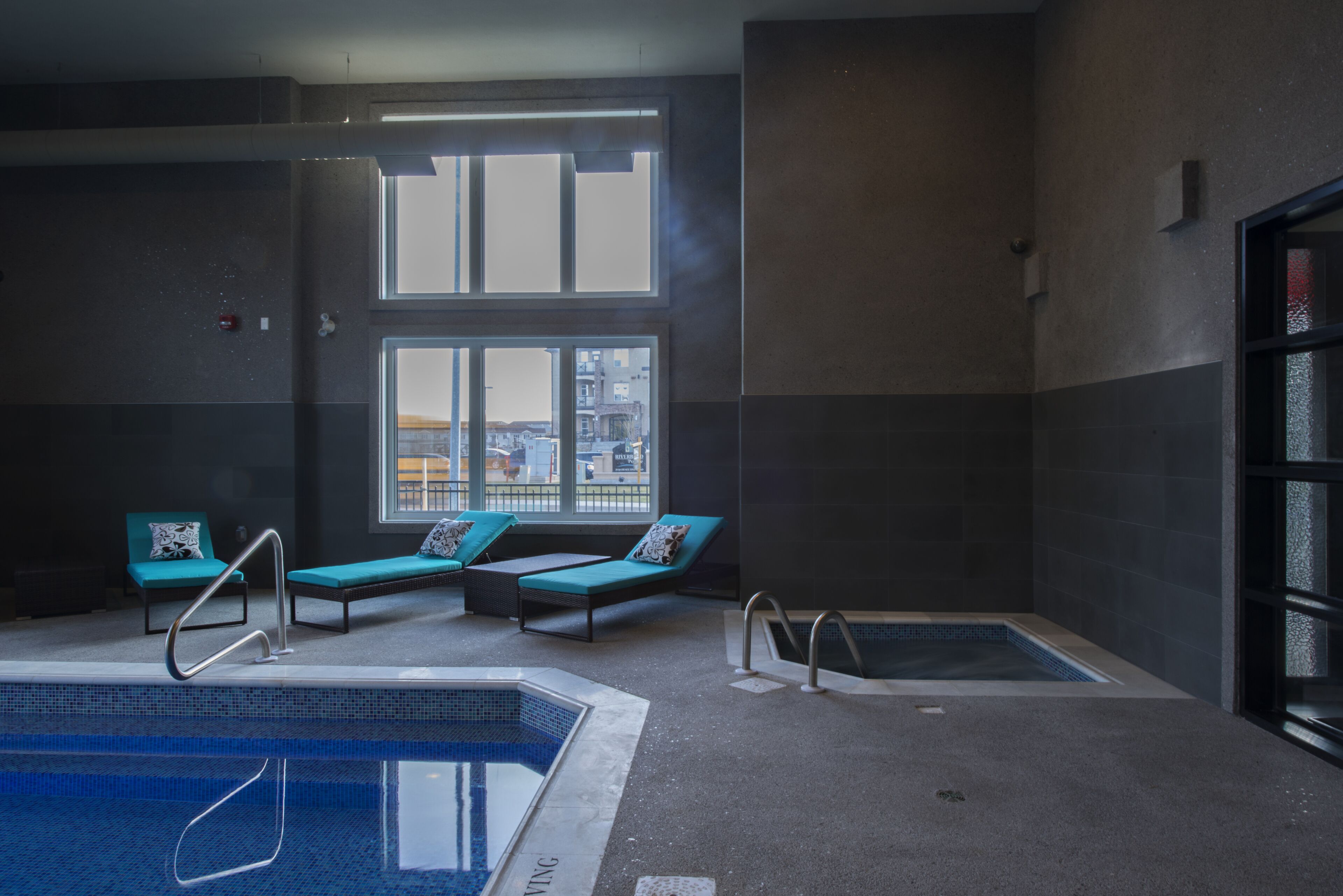 An indoor swimming pool with lounge chairs and a view of the city through large windows.