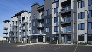 A multi-story residential building with balconies, a parking lot, and a clear sky. - NEW Aura Newly built and spacious 2 bed, 2 bathrooms (Regina)
