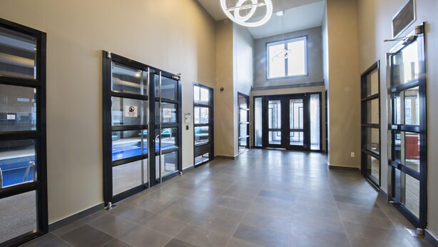 A spacious hallway with glass doors leading to a pool area, a large window, and a modern light fixture. - NEW Aura Newly built and spacious 2 bed, 2 bathrooms (Regina)