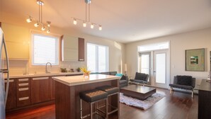 A modern kitchen with a central island, wooden cabinets, and a dining area with a sofa and coffee table. - NEW Aura Newly built and spacious 2 bed, 2 bathrooms (Regina)