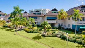 A row of beachfront villas with a well-maintained lawn, palm trees, and a clear blue sky.