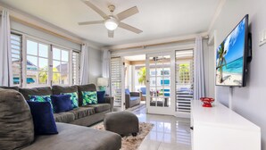 A spacious living room with a grey sofa, blue and green patterned pillows, a white coffee table, and a red decorative item.