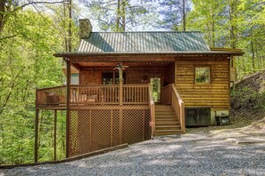 Eine Holzhütte mit Balkon, Treppe und einem Schotterweg, umgeben von Bäumen.