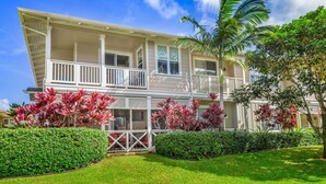 A two-story house with a balcony, surrounded by well-maintained lawns and tropical plants. - Leilani Villa: Gardenview Condo on Kauai's North Shore w/ Pool, Spa & AC (Princeville)