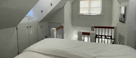 Een slaapkamer met een schuine kap, een bed, een bureau en een raam.