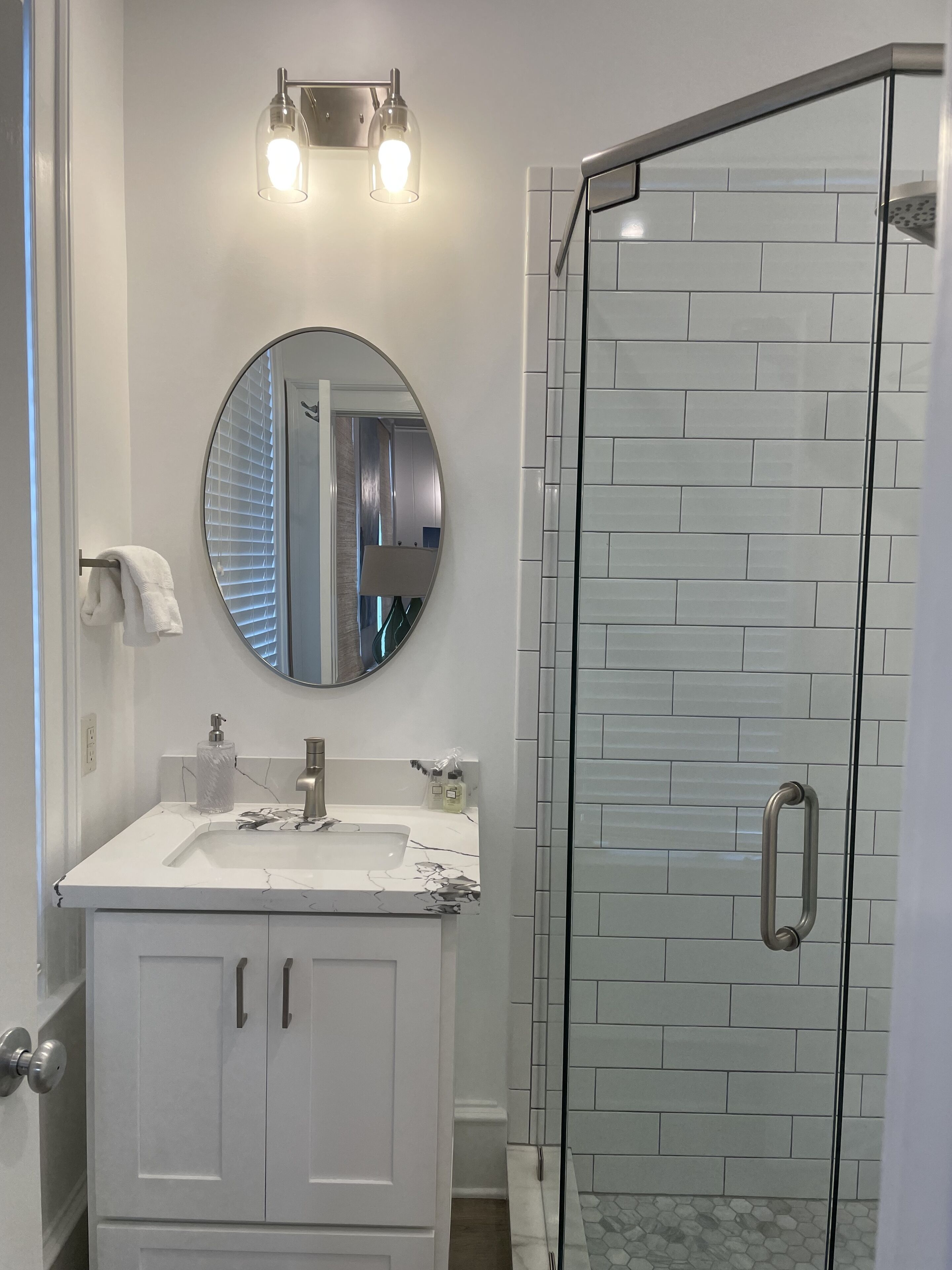 Un baño con tocador blanco, espejo redondo y cabina de ducha de vidrio.