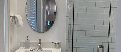 Un baño con tocador blanco, espejo redondo y cabina de ducha de vidrio.