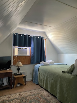 Cozy attic bedroom with a large bed, television, and decorative rug.