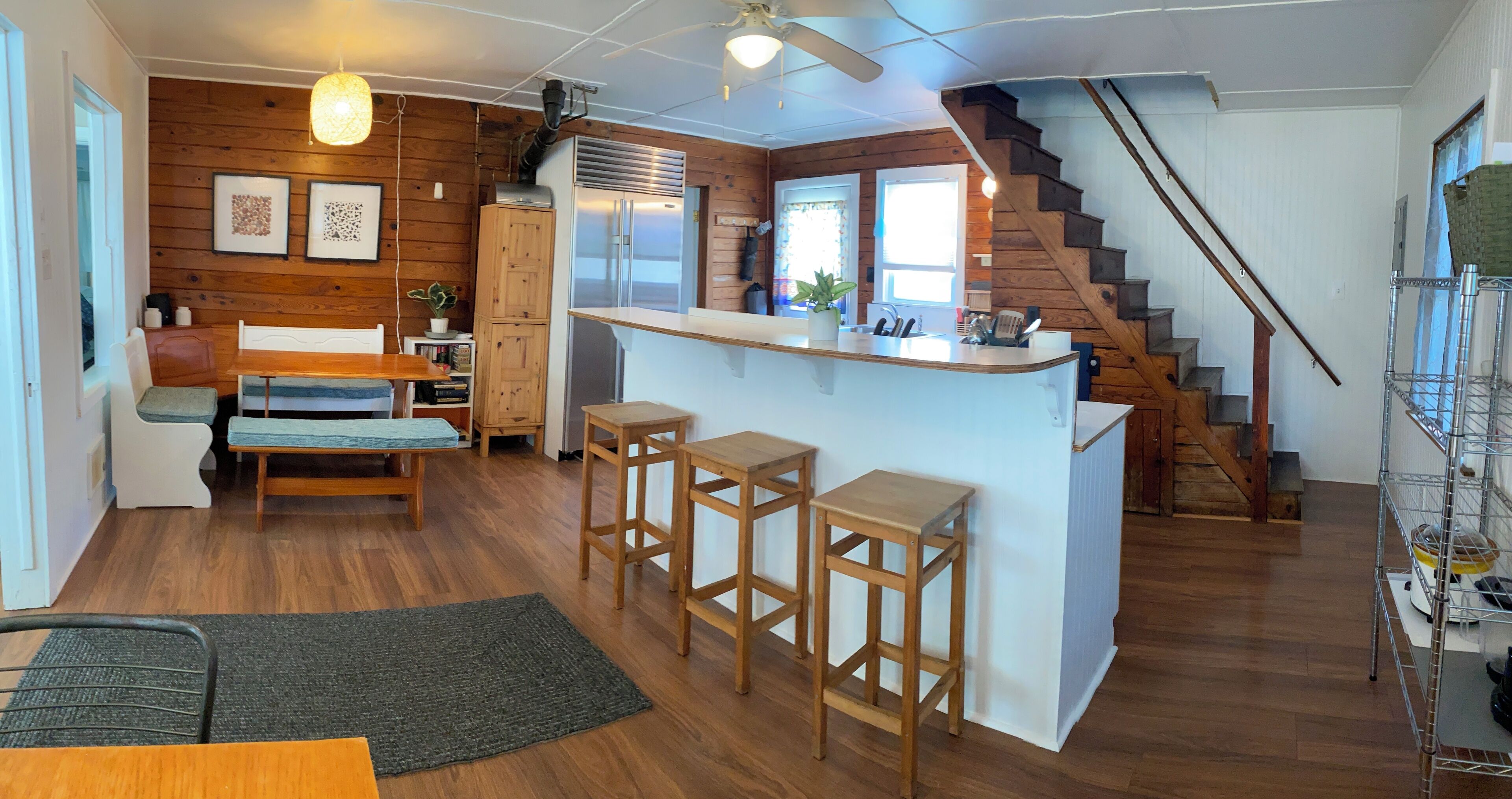 A kitchen with wooden flooring, a central island with stools, a refrigerator, and a staircase leading to another level.