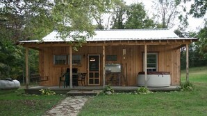 Un chalet rustique en bois, doté d’un porche, d’un chemin d’accès en pierre menant à l’entrée et d’un petit espace extérieur aménagé pour s’asseoir.