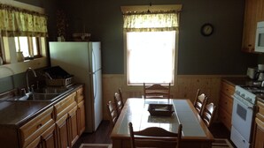 Une cuisine avec des meubles de rangement en bois, un réfrigérateur, une cuisinière, une table à manger avec des chaises et une fenêtre avec des rideaux.